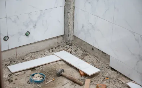 Travaux de pose de faience salle de bain : des carreaux de marbre blanc sont prêts à être installés, avec des outils au sol.