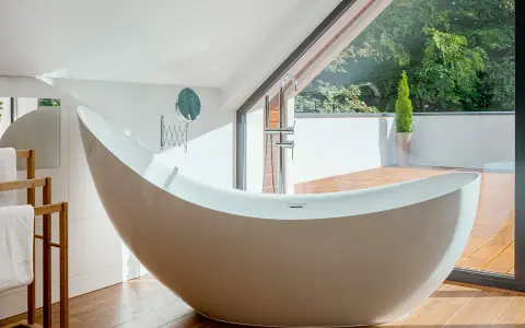 Baignoire design en matière composite, avec robinetterie chromée, devant une grande baie vitrée donnant sur un jardin luxuriant.