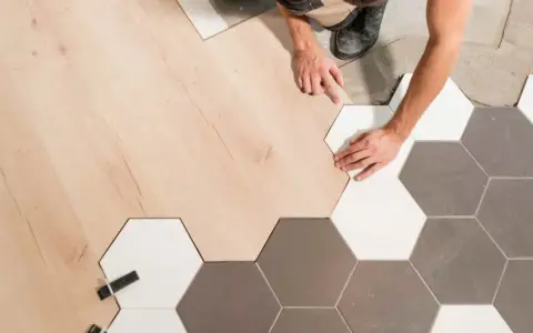 Pose d'un parquet bois clair et de carreaux hexagonaux gris et blancs. La jonction parquet carrelage est en cours de réalisation par un artisan.