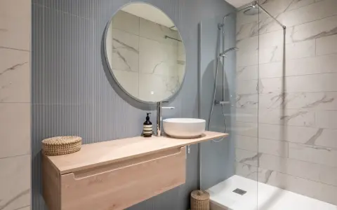 Aménagement petite salle de bain : meuble suspendu en bois clair, vasque ronde, miroir rond, douche à l'italienne.