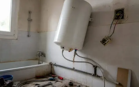 Un chauffe-eau blanc est en cours de branchement dans une salle de bain. Des outils sont posés sur le sol.