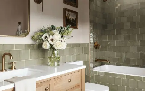 Élégante salle de bain verte avec carrelage texturé, vasque en bois, bouquet de fleurs blanches et robinetterie dorée.