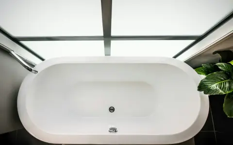 Vue aérienne d'une baignoire blanche moderne, prête à accueillir un bain relaxant. La contenance baignoire est généreuse, sous un puits de lumière.