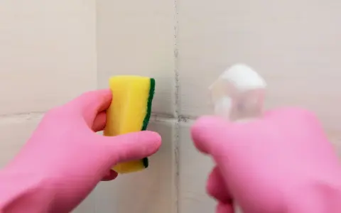 Main rose gantée tient une éponge jaune pour nettoyer une tache sur carrelage qui ne part pas.