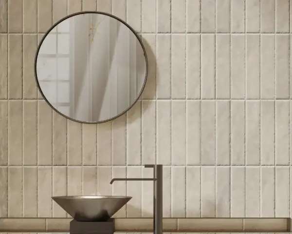 Un lavabo moderne et un miroir rond se reflètent sur un mur de toilette carrelage aux tons sable.