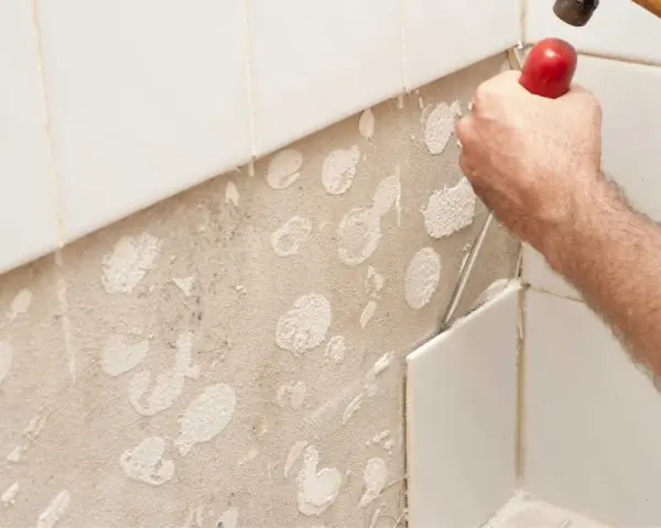 Main d'un bricoleur en pleine action pour enlever carrelage mural avec un burin et un marteau. La surface est prête pour un nouveau revêtement.