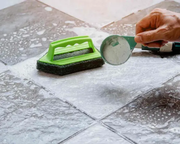 Nettoyer un carrelage mat et poreux avec une brosse et une poudre nettoyante.