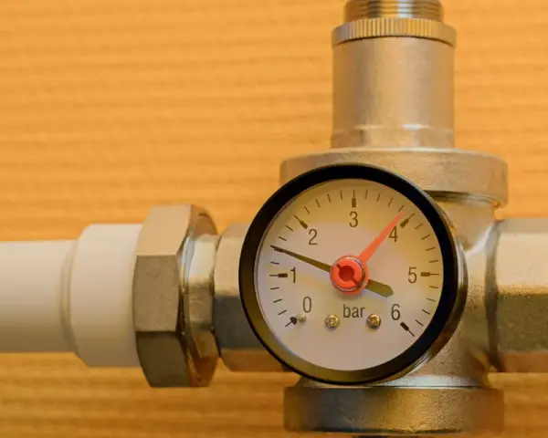 Un réducteur de pression d'eau avec un manomètre indiquant 1 bar. L'appareil est monté sur un tuyau blanc.