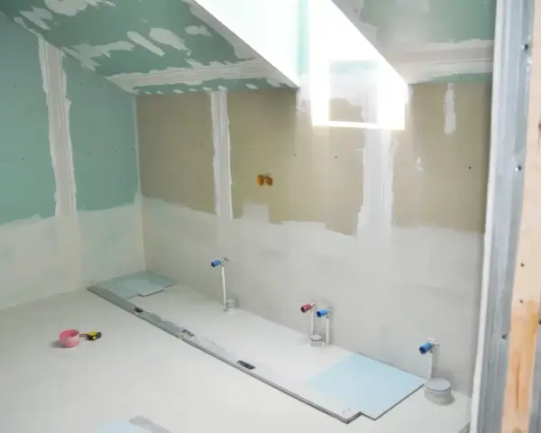 Chantier de salle de bain : murs en plaques de plâtre, tuyauterie apparente, niveau à bulle et outils au sol. Travaux d'isolation salle de bain en cours.
