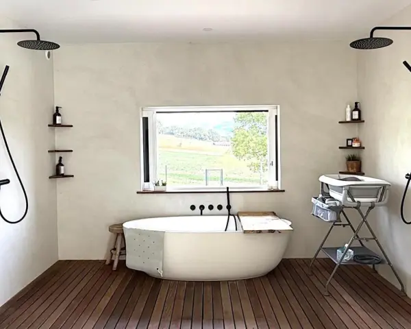 Une **salle de bain intemporelle** avec baignoire îlot, deux douches murales, et une vue sur la campagne.