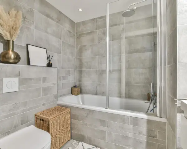 Salle de bain entierement carrelée de gris, avec baignoire, douche, lavabo et WC. Un panier en osier et des herbes séchées apportent une touche naturelle.