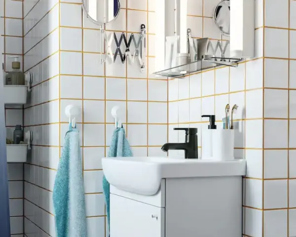Salle de bain moderne avec carrelage blanc et joints dorés, évier, robinetterie noire et accessoires. Idéal pour un plancher chauffant avec un joint de 2mm.