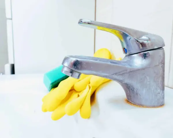 Gants jaunes et éponge verte prêts pour nettoyer robinetterie entartrée.