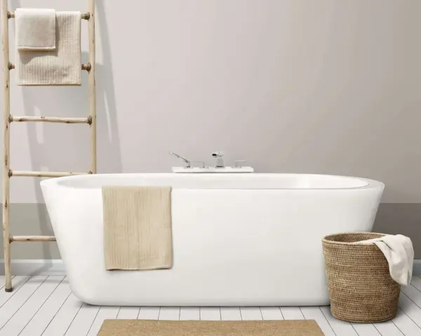 Baignoire moderne avec robinetterie chromée. Un porte-serviettes en bois et un panier en osier complètent l'ensemble, suggérant un émail baignoire poreux à l'aspect naturel.