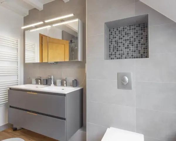 Salle de bain moderne avec double vasque, radiateur blanc et un choix carrelage gris subtil, agrémenté d'une niche décorative en mosaïque.