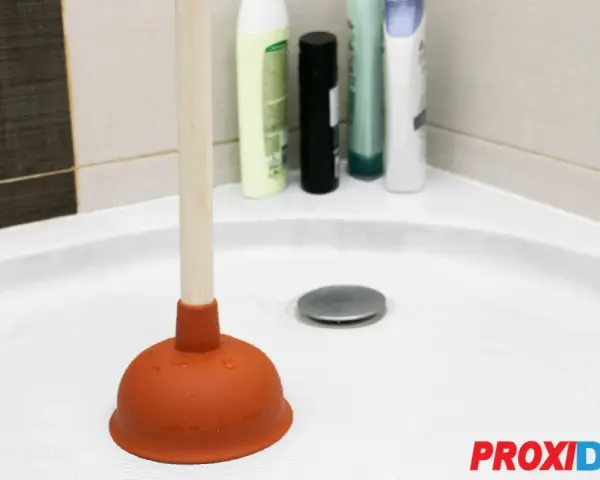 Plongeur dans une douche bouchée avec de l'eau stagnante. Des bouteilles de shampoing sont visibles en arrière-plan.