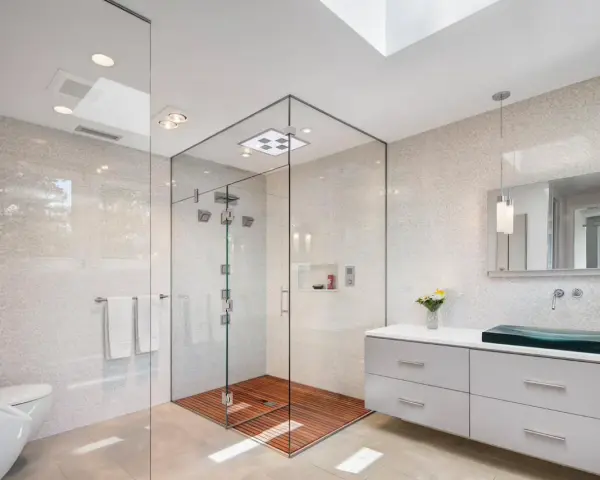 Salle de bain moderne avec douche italienne spacieuse, sol en bois, murs en mosaïque et lavabo design.