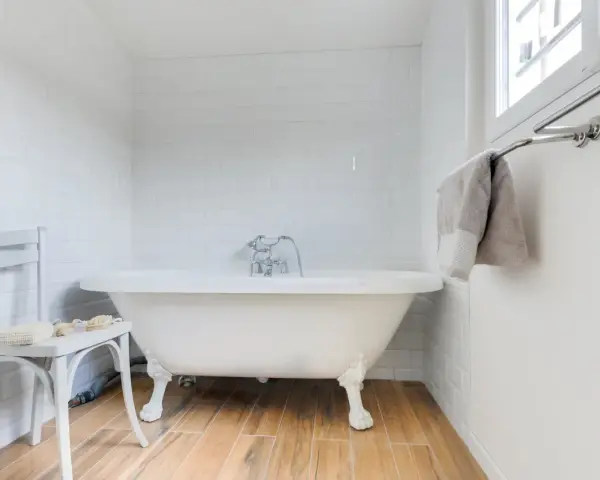 Baignoire îlot blanche sur pieds, robinetterie argentée. La hauteur baignoire est standard, avec un petit tabouret à côté.