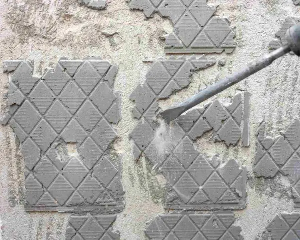 Outil de burinage en action pour enlever colle carrelage sur un mur en béton.