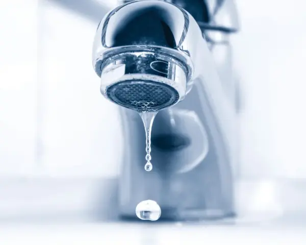 Gouttelettes d'eau tombant d'un robinet de salle de bain qui fuit. Un petit désagrément qui coûte cher.