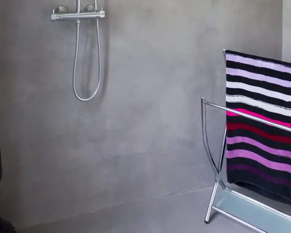 Salle de bain béton ciré aux tons gris, avec une douche chromée et un porte-serviettes orné d'une serviette rayée.