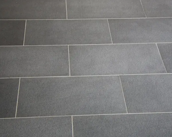 Détail d'un sol en carrelage gris anthracite, avec un joint carrelage couleur crème qui souligne la pose rectiligne.