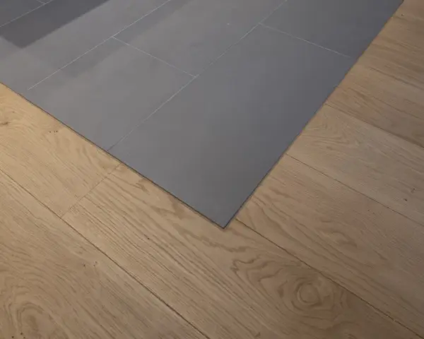 Un coin de sol où le carrelage gris imitation parquet rencontre un parquet en bois naturel. La couleur du joint du carrelage est discrète.