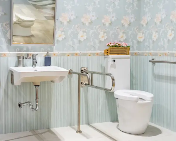 Salle de bain senior : lavabo suspendu, WC avec barre d'appui rabattable et barre d'appui murale pour plus de sécurité.