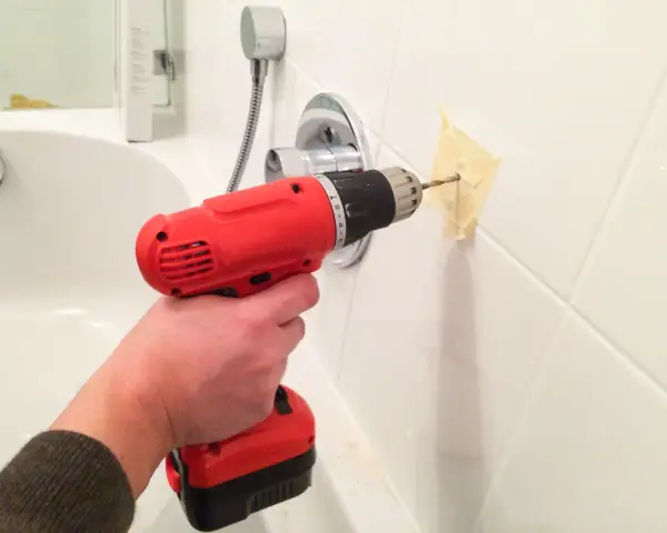 Main tenant utilise une perceuse pour percer le carrelage de la salle de bain, afin d'y fixer un accessoire.