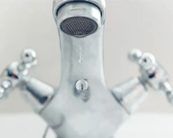 Gouttes d'eau tombant d'un robinet chromé. Comprendre la différence entre mitigeur et mélangeur pour une meilleure gestion de l'eau.