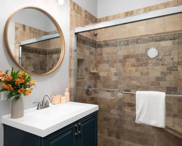 Salle de bain moderne avec douche carrelée, lavabo et miroir rond. Idéal pour nettoyer VMC et profiter d'un espace sain.