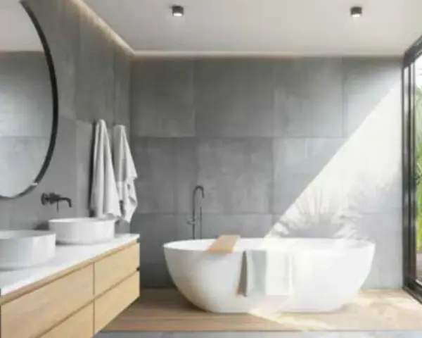 Salle de bain moderne avec baignoire îlot, double vasque et grande fenêtre donnant sur la végétation. L'étanchéité entre bac à douche et mur est assurée par des joints discrets.