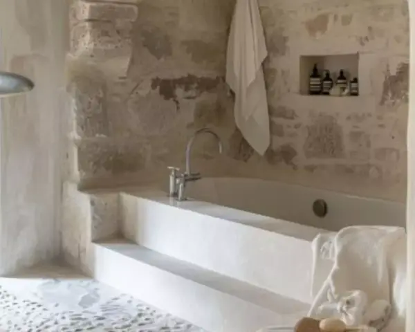 Une **salle de bain méditerranéenne** avec baignoire en pierre brute, robinetterie moderne et serviette blanche suspendue. Ambiance zen.