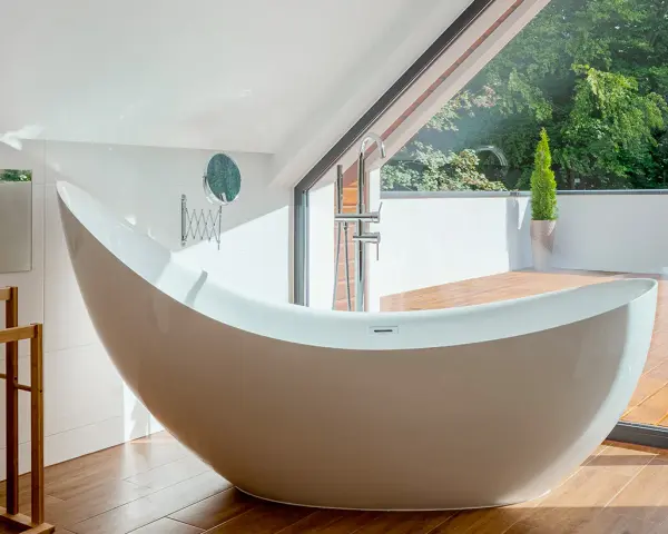 Baignoire design en matière composite, avec robinetterie chromée, devant une grande baie vitrée donnant sur un jardin luxuriant.