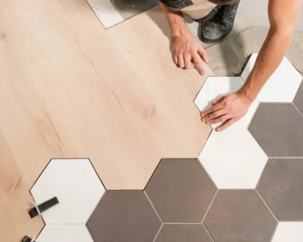 Pose d'un parquet bois clair et de carreaux hexagonaux gris et blancs. La jonction parquet carrelage est en cours de réalisation par un artisan.