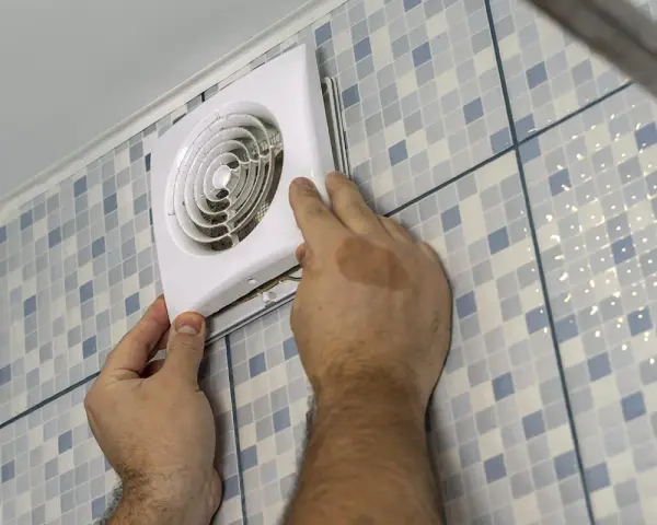 Mains d'un homme installant un ventilateur, une étape clé pour une bonne installation VMC dans une salle de bain carrelée.