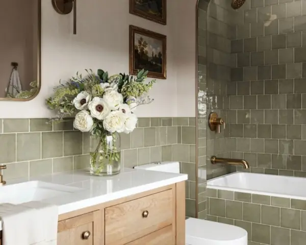 Élégante salle de bain verte avec carrelage texturé, vasque en bois, bouquet de fleurs blanches et robinetterie dorée.