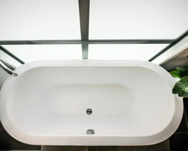 Vue aérienne d'une baignoire blanche moderne, prête à accueillir un bain relaxant. La contenance baignoire est généreuse, sous un puits de lumière.
