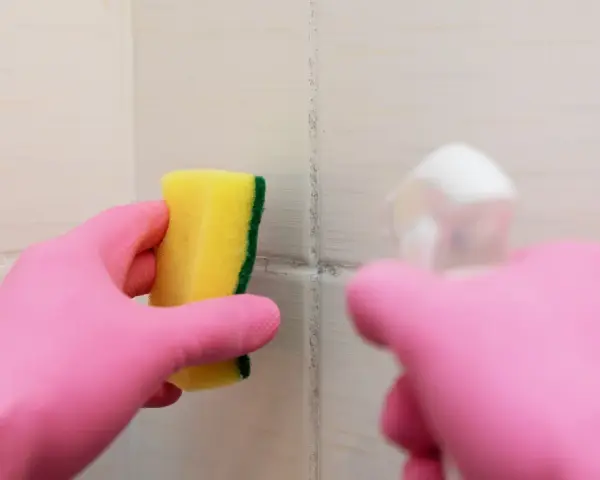 Main rose gantée tient une éponge jaune pour nettoyer une tache sur carrelage qui ne part pas.