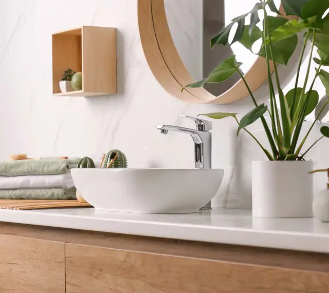 Plan de travail de salle de bain moderne avec vasque, robinetterie chromée, serviettes pliées et plante verte. La hauteur du plan de travail est idéale.