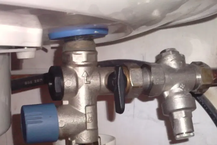Un réducteur de pression, comme ce dispositif métallique avec une poignée noire, sert à réguler la pression de l'eau dans une installation.