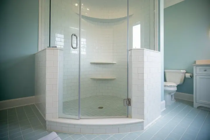 Salle de bain avec carrelage bleu pâle et une douche d'angle. Ce receveur de douche à éviter, avec ses étagères peu pratiques, est un cauchemar à nettoyer.
