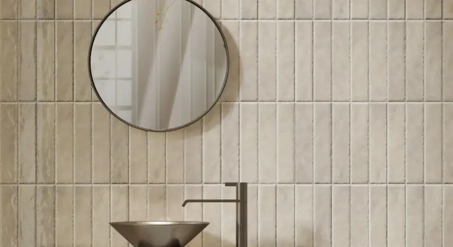 Un lavabo moderne et un miroir rond se reflètent sur un mur de toilette carrelage aux tons sable.