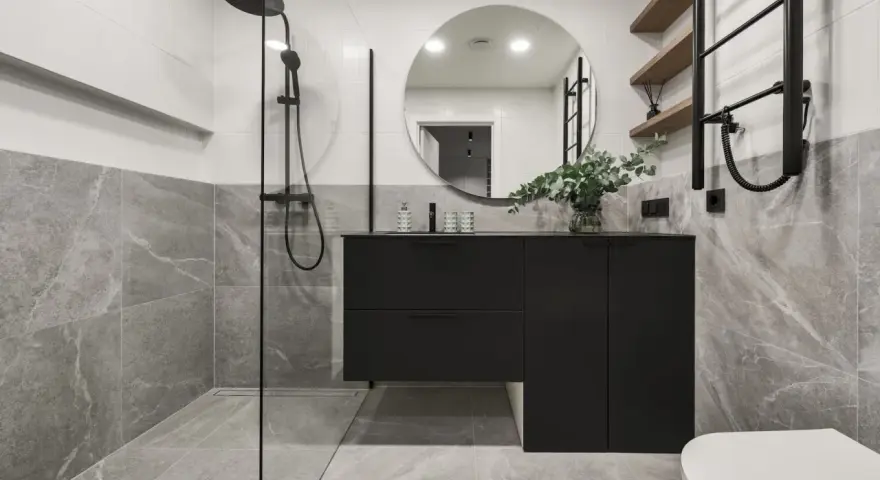 Salle de bain moderne avec douche à l'italienne, meuble suspendu noir, miroir rond et carrelage effet marbre. La construction de cette salle de bain est soignée.