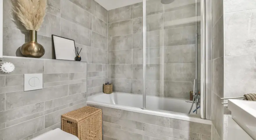 Salle de bain entierement carrelée de gris, avec baignoire, douche, lavabo et WC. Un panier en osier et des herbes séchées apportent une touche naturelle.