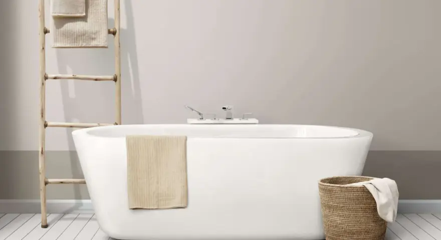 Baignoire moderne avec robinetterie chromée. Un porte-serviettes en bois et un panier en osier complètent l'ensemble, suggérant un émail baignoire poreux à l'aspect naturel.