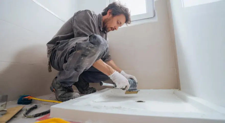 Un ouvrier prépare le sol pour installer un receveur de douche. Il utilise une ponceuse pour assurer une surface plane, essentielle pour le collage.