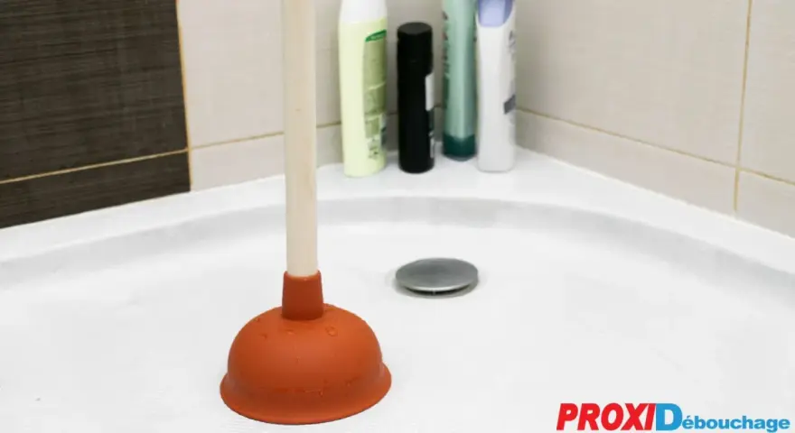 Plongeur dans une douche bouchée avec de l'eau stagnante. Des bouteilles de shampoing sont visibles en arrière-plan.