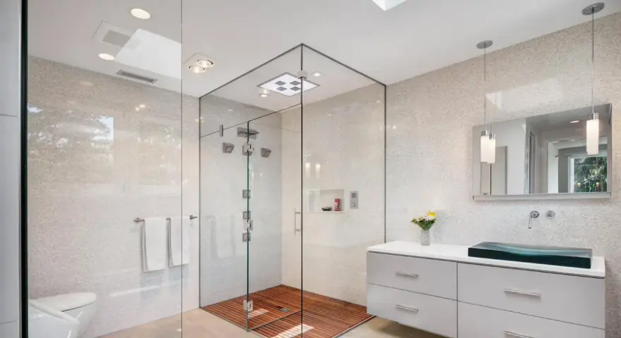 Salle de bain moderne avec douche italienne spacieuse, sol en bois, murs en mosaïque et lavabo design.