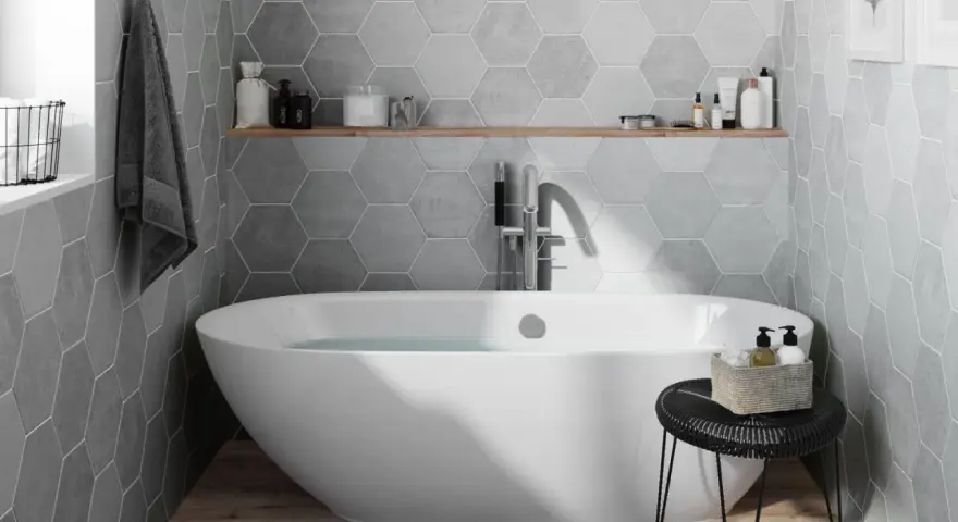 Salle de bain moderne avec baignoire îlot, carrelage mural hexagonal gris et étagère en bois.